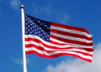 An American flag on a flagpole waving against a blue sky with a few clouds.